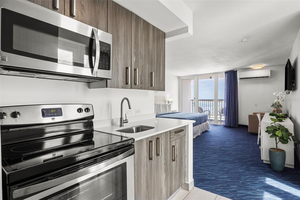 A kitchen with wood-look cabinets and stainless appliances overlooks a bedroom with a balcony view — 6165 ISLA VERDE AVE. UNIT 1550, CAROLINA, PR