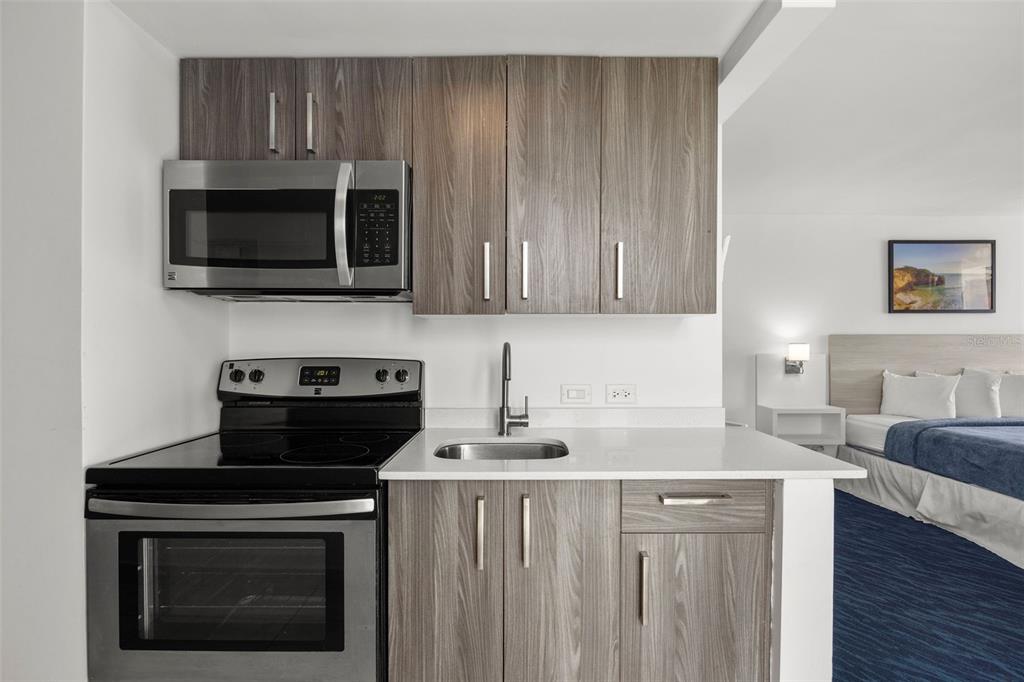 A kitchenette with wood-grain cabinets, stainless steel appliances, and a white countertop next to a bedroom — 6165 ISLA VERDE AVE. UNIT 1550, CAROLINA, PR