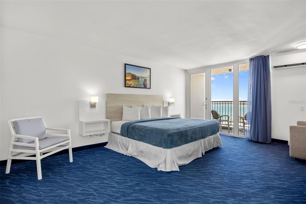 A bedroom features a king bed, blue carpeting, and a balcony overlooking the ocean — 6165 ISLA VERDE AVE. UNIT 1550, CAROLINA, PR