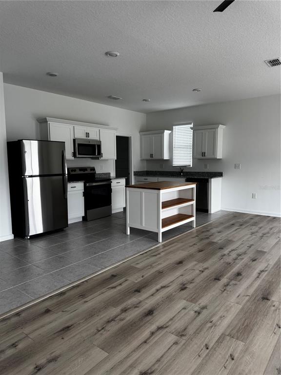 A kitchen features white cabinets, stainless steel appliances, a center island, and gray tile flooring — 2210 RAVEN RIDGE ROAD, MINNEOLA, FL