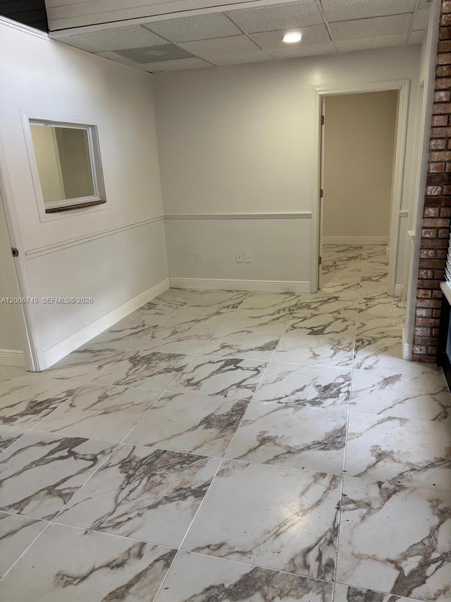 A room with white marble-patterned tile flooring, light gray walls, and a brick accent wall — 5327 Commercial Way # B105, FL 34606, FL