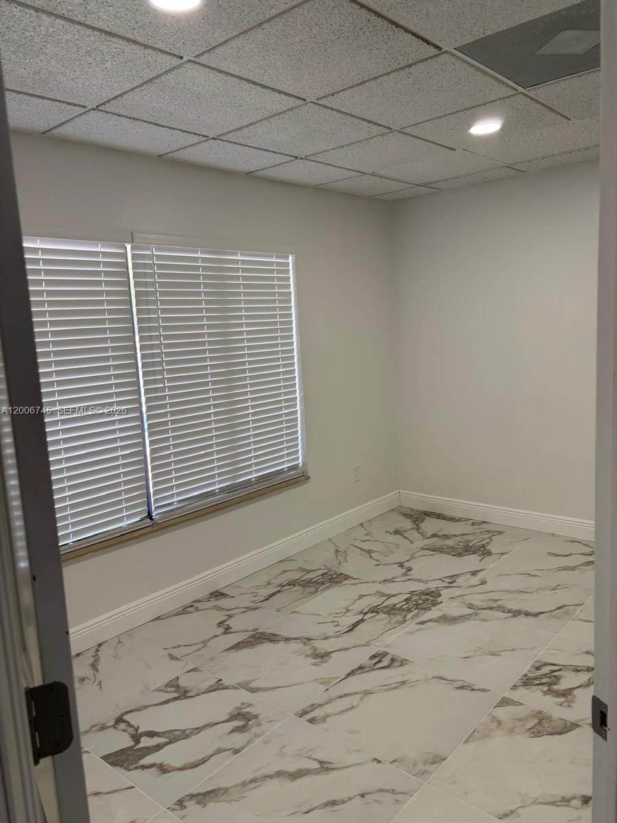 An empty room features white marble-patterned tile flooring, light gray walls, and a drop ceiling — 5327 Commercial Way # B105, FL 34606, FL