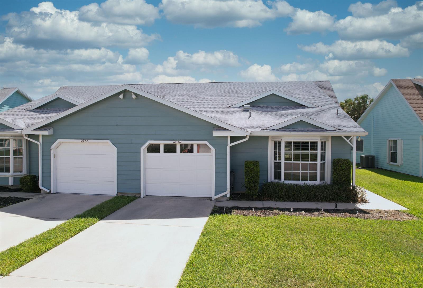 A blue duplex home features two white garage doors and a bay window — 4074 Gator Trace Road, Fort Pierce FL 34982, FORT PIERCE, FL