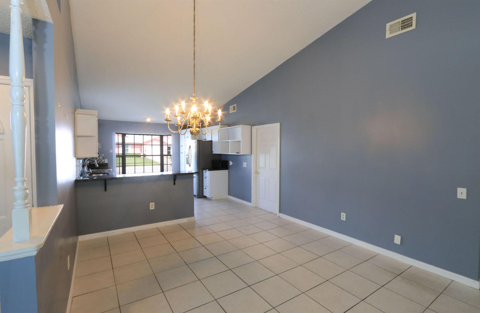A dining area with tile floors, blue walls, a chandelier, and an open kitchen — 4074 Gator Trace Road, Fort Pierce FL 34982, FORT PIERCE, FL