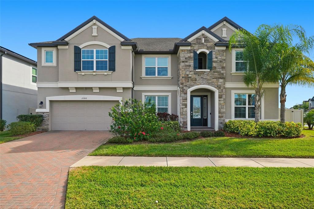 A two-story suburban home with a stone facade, a brick driveway, and a green lawn — 11002 SUNDRIFT DRIVE, TAMPA, FL