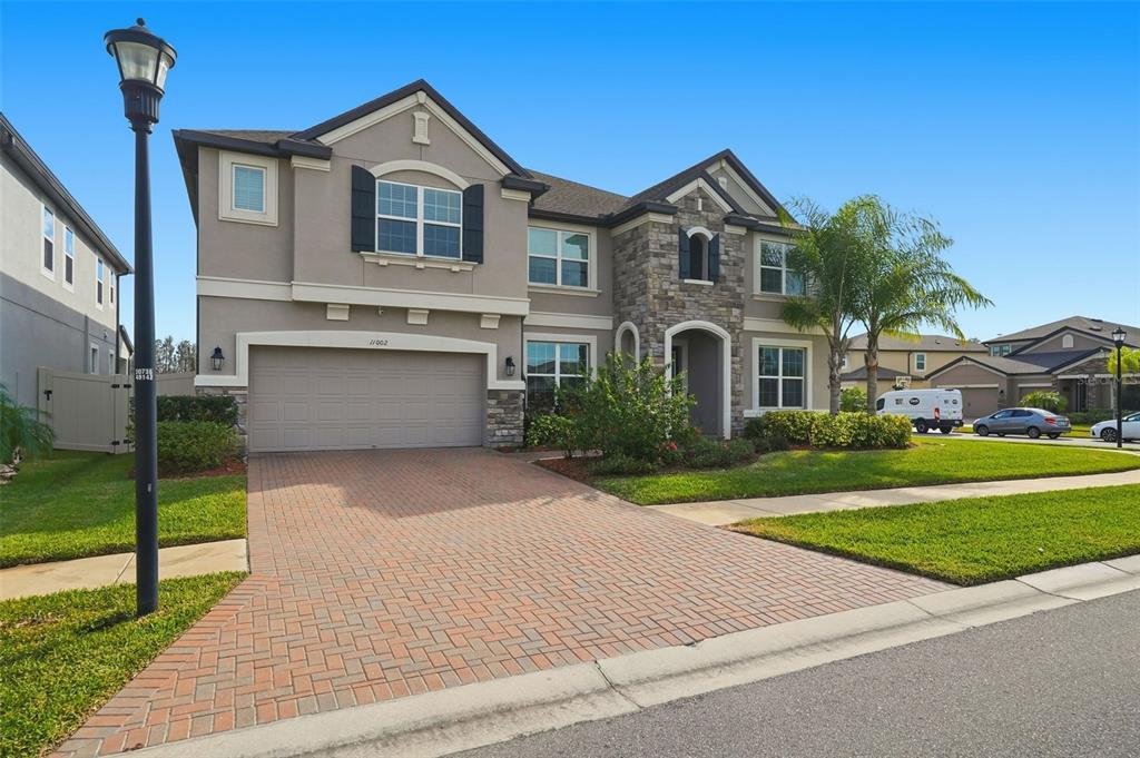 A two-story suburban house with a stone facade, stucco exterior, and a brick paver driveway — 11002 SUNDRIFT DRIVE, TAMPA, FL