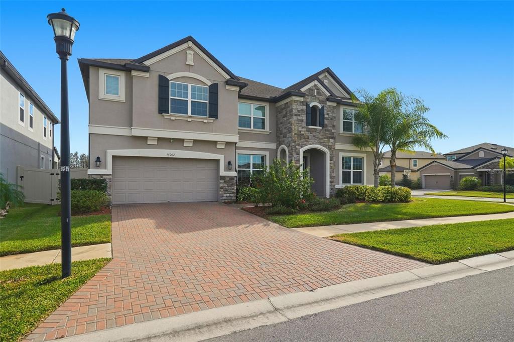 A two-story suburban house features a stone facade, a brick driveway, and a two-car garage — 11002 SUNDRIFT DRIVE, TAMPA, FL