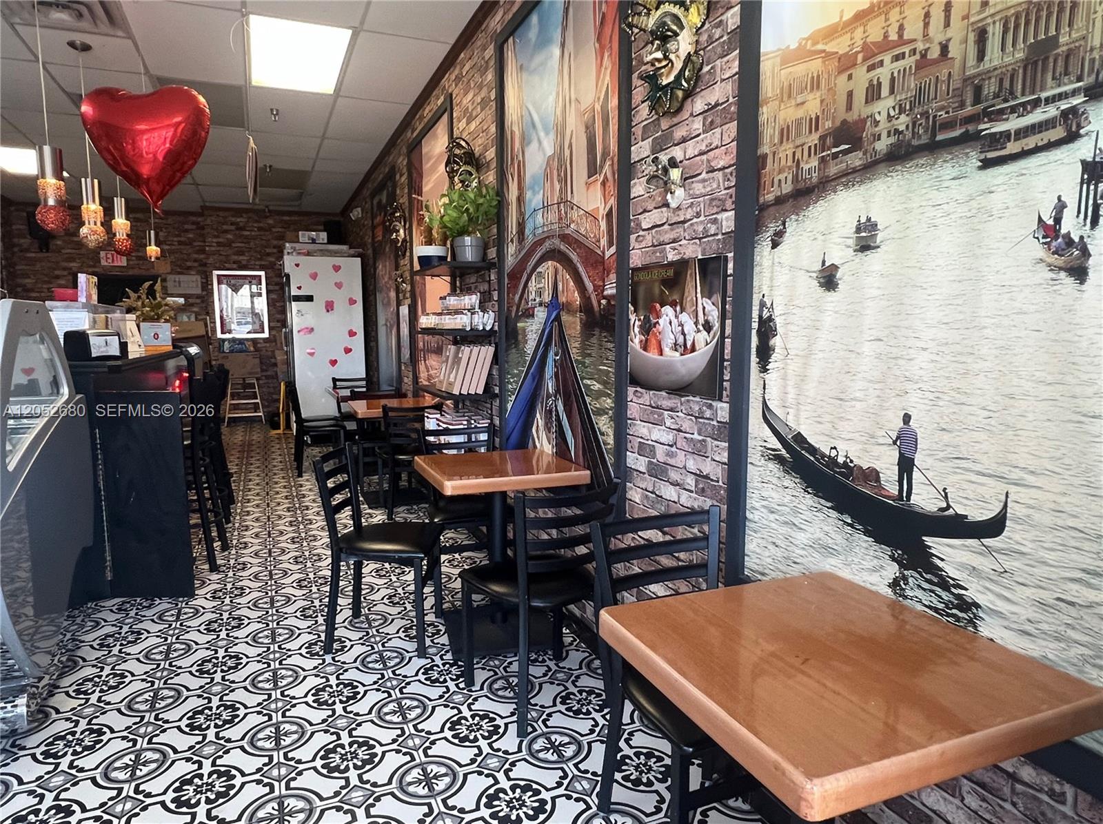 A small cafe features patterned tile floors, brick-style walls, and large murals of Venice — KENDALL, FL