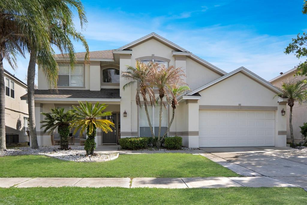A two-story suburban house features a beige exterior, a two-car garage, and palm trees — 2735 SCARBOROUGH DRIVE, KISSIMMEE, FL