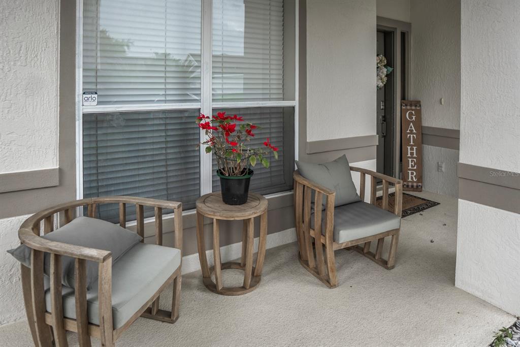 A covered porch features two wooden armchairs, a small round table, and a potted plant — 2735 SCARBOROUGH DRIVE, KISSIMMEE, FL
