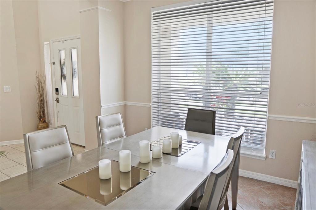 A dining room features a metallic table with pillar candles, silver chairs, and large blinds — 2735 SCARBOROUGH DRIVE, KISSIMMEE, FL