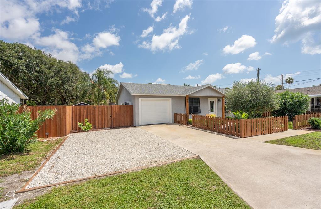 A single-story house with a gravel driveway, a one-car garage, and a wooden picket fence — 208 TRADE WIND LANE, ST AUGUSTINE BEACH, FL