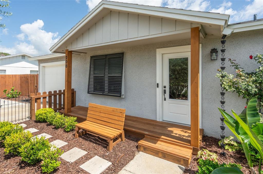 A house exterior features a wooden porch, a bench, a front door, and landscaping — 208 TRADE WIND LANE, ST AUGUSTINE BEACH, FL