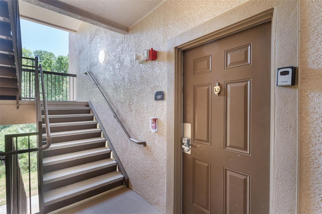 A brown apartment door with a digital lock is located next to an outdoor staircase — 1375 TUSCANA LANE UNIT 1207, DAVENPORT, FL