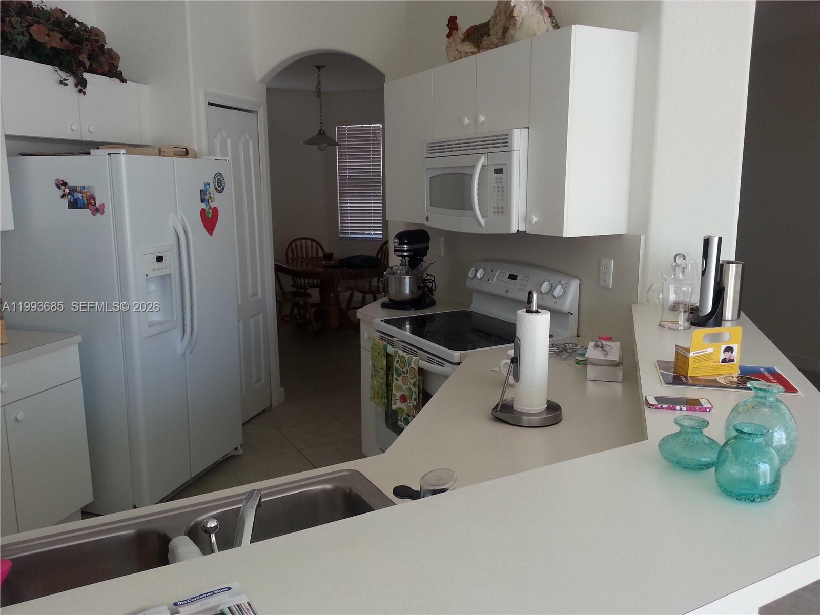 A kitchen features white cabinetry, a white refrigerator, a stainless steel sink, and a breakfast bar — 11050 NW 86th Ter, Doral FL 33178, DORAL, FL