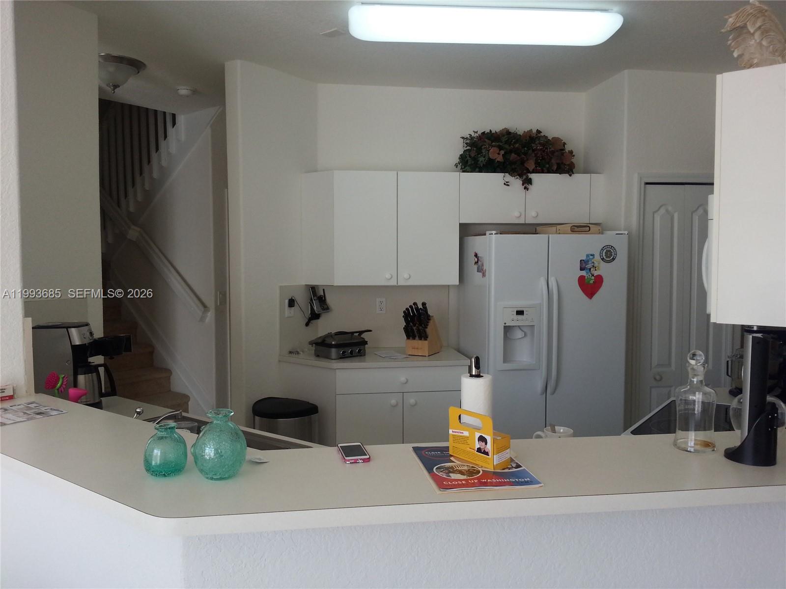 A kitchen features white cabinets, a refrigerator, and a breakfast bar with decorative glass vases — 11050 NW 86th Ter, Doral FL 33178, DORAL, FL