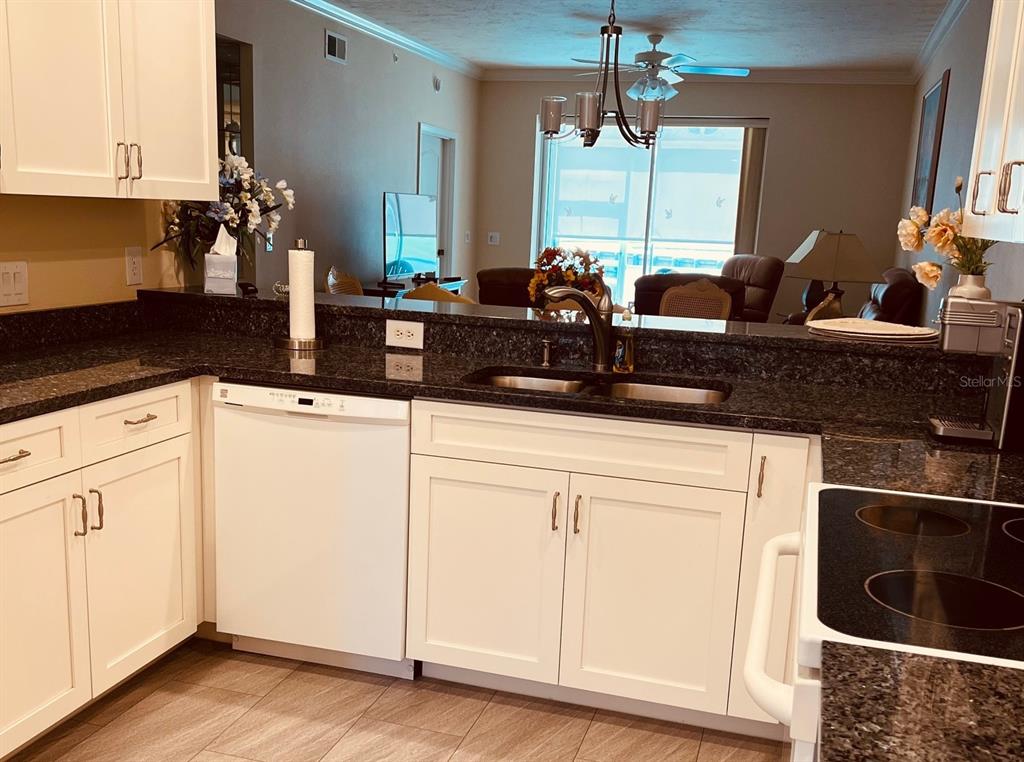 A kitchen with white cabinets, dark granite countertops, and a view into the living area — 4639 CHAPEL HILL DRIVE UNIT 2912, SARASOTA, FL
