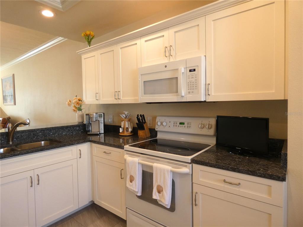 A kitchen features white cabinets, dark granite countertops, and a white electric range — 4639 CHAPEL HILL DRIVE UNIT 2912, SARASOTA, FL
