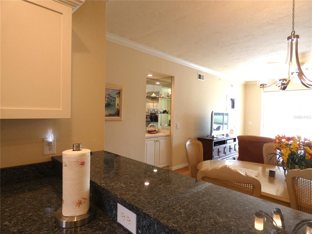 A kitchen counter with granite countertops overlooks a dining area and a mirrored wet bar — 4639 CHAPEL HILL DRIVE UNIT 2912, SARASOTA, FL