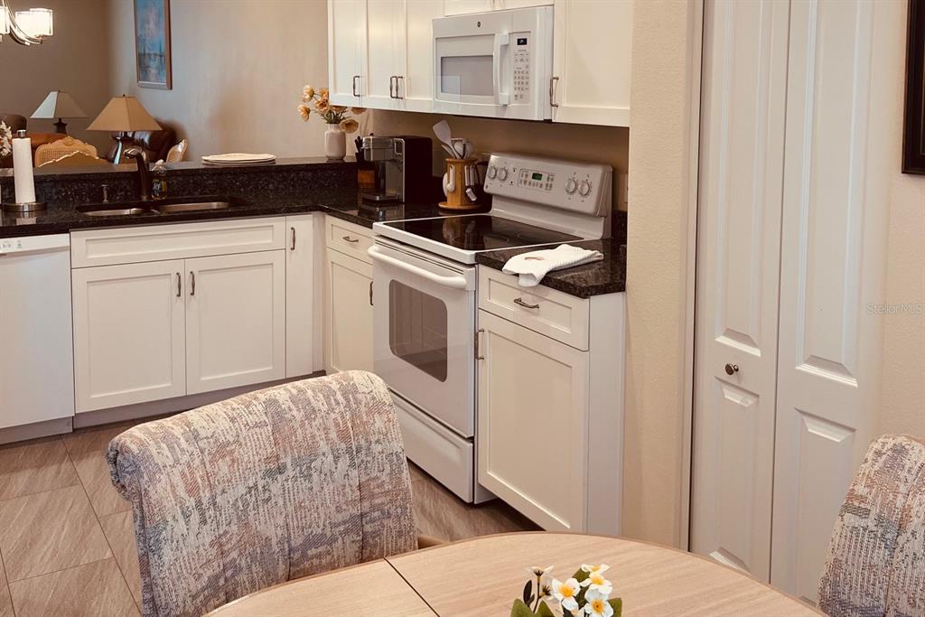 A kitchen features white cabinets, dark countertops, white appliances, and a dining area in the foreground — 4639 CHAPEL HILL DRIVE UNIT 2912, SARASOTA, FL