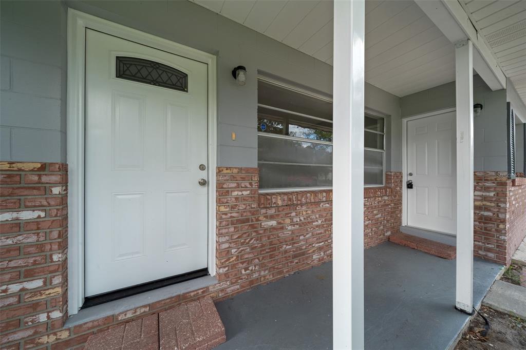 A covered porch features two white entry doors, gray walls, and a red brick base — 2100 NE 52ND STREET, OCALA, FL