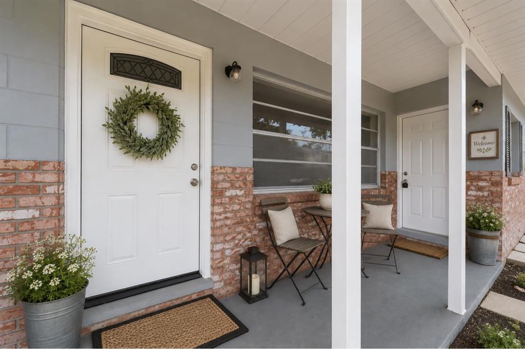 A covered front porch features two white doors, brick siding, and outdoor seating — 2100 NE 52ND STREET, OCALA, FL