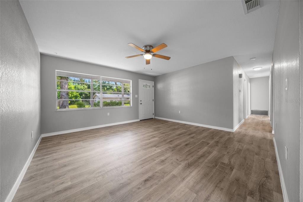A living room with gray walls, wood-look flooring, a ceiling fan, and a front door — 2100 NE 52ND STREET, OCALA, FL
