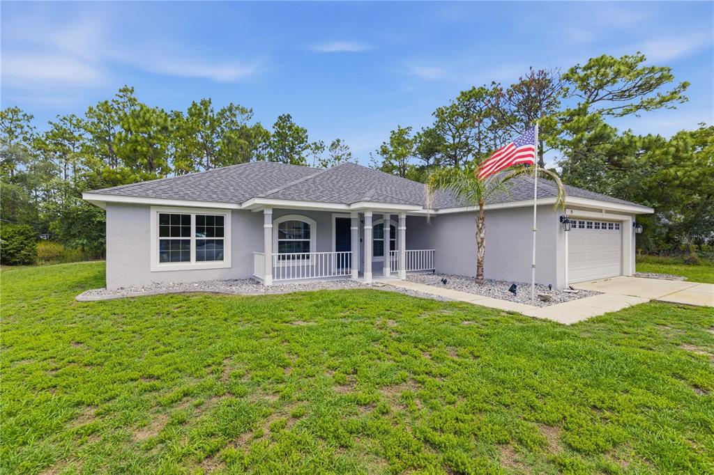 A single-story gray house with a white porch railing, a two-car garage, and a flag pole — 35 SPECEBERRY CIRCLE, HOMOSASSA, FL