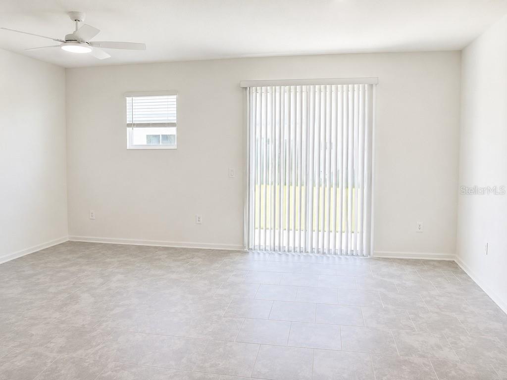 An empty room with light gray tile flooring, a ceiling fan, and sliding glass doors — 7604 STONE CREEK TRAIL, KISSIMMEE, FL