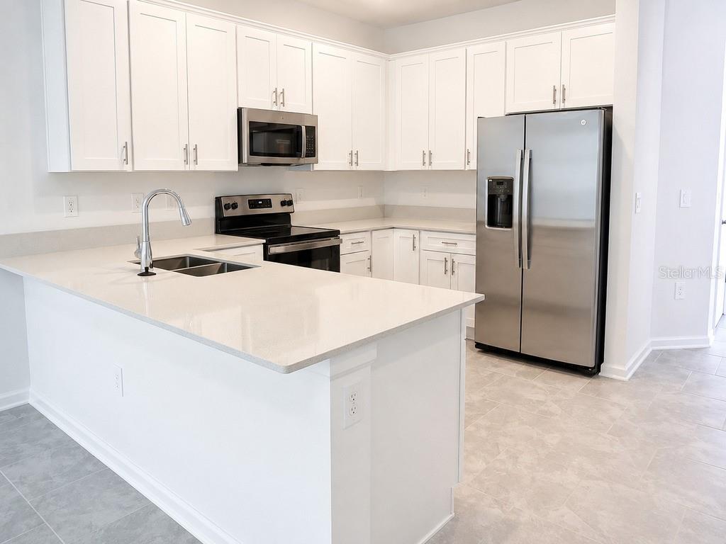 A modern kitchen features white cabinets, stainless steel appliances, and a quartz-topped island — 7604 STONE CREEK TRAIL, KISSIMMEE, FL