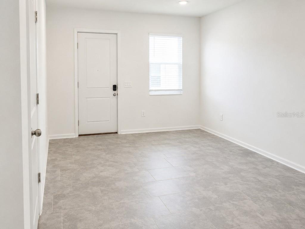 An empty room with gray tile flooring, white walls, a single window, and a door — 7604 STONE CREEK TRAIL, KISSIMMEE, FL