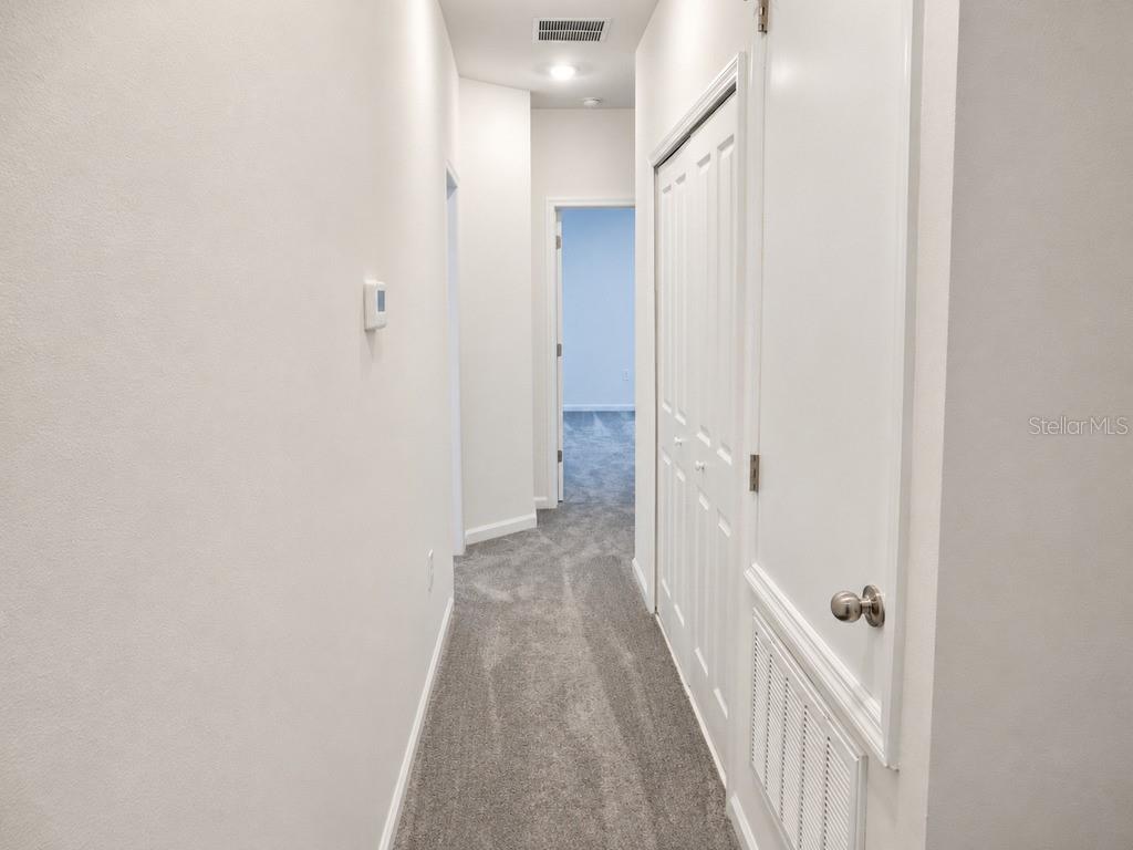 A hallway with gray carpeting leads to a doorway, featuring a white closet door — 7604 STONE CREEK TRAIL, KISSIMMEE, FL