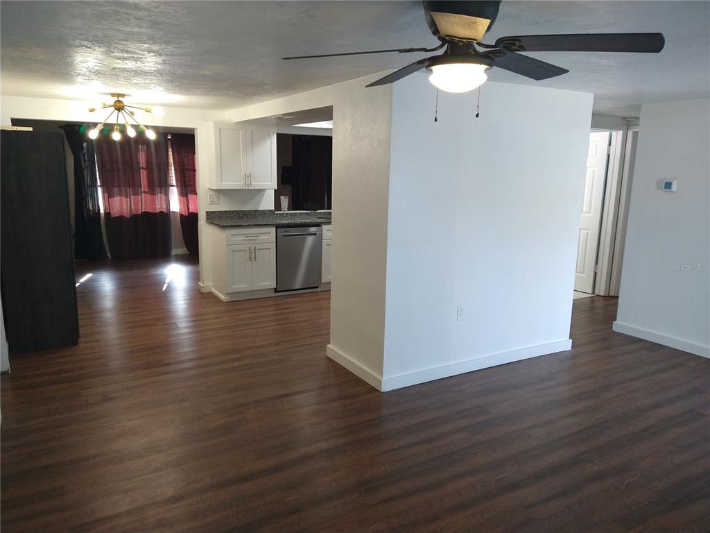 An open-concept living area features wood-look flooring, a ceiling fan, and a white kitchen — 12910 COLLEGE HILL DRIVE, HUDSON, FL
