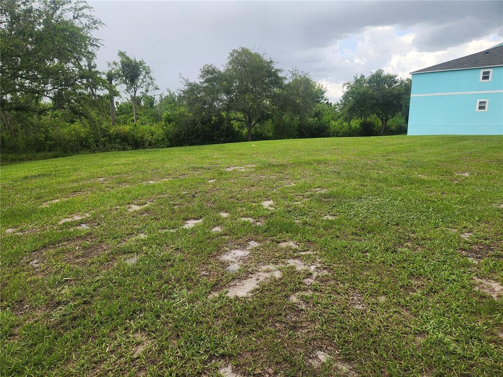 A grassy, vacant lot sits next to a light blue multi-story building under a cloudy sky — 3134 SUN LAKE COURT UNIT B, KISSIMMEE, FL