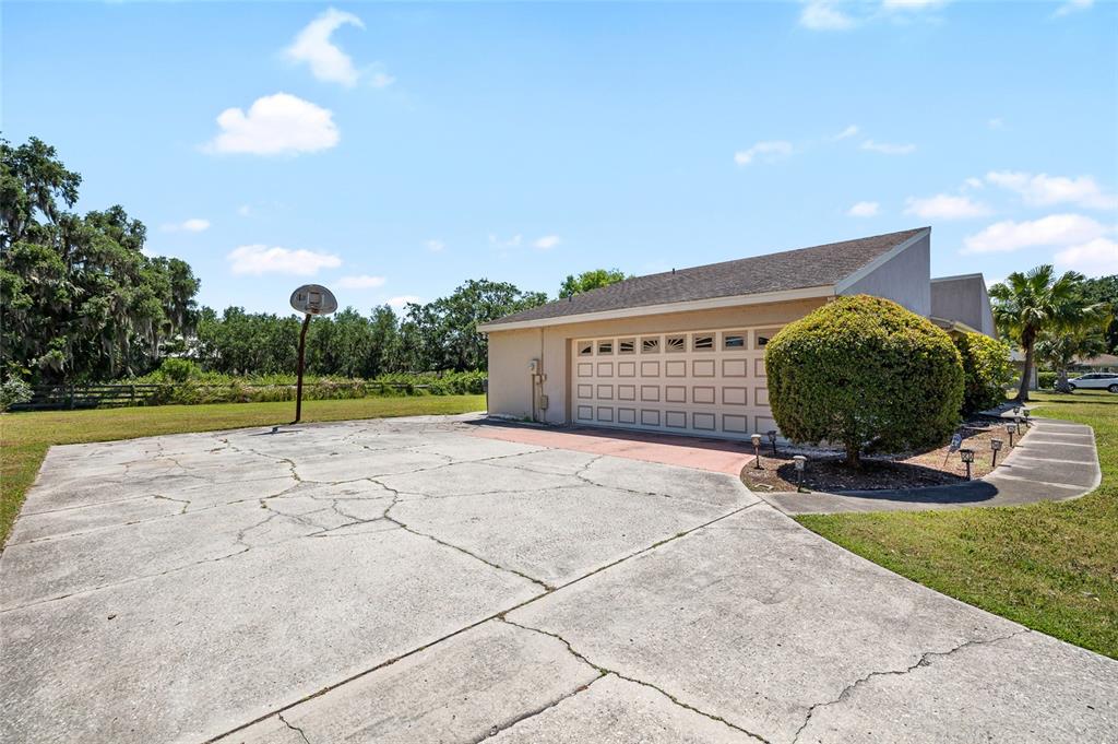 A concrete driveway with cracks leads to a two-car garage beside a large bush — 34 MISTY MEADOW LANE, MULBERRY, FL