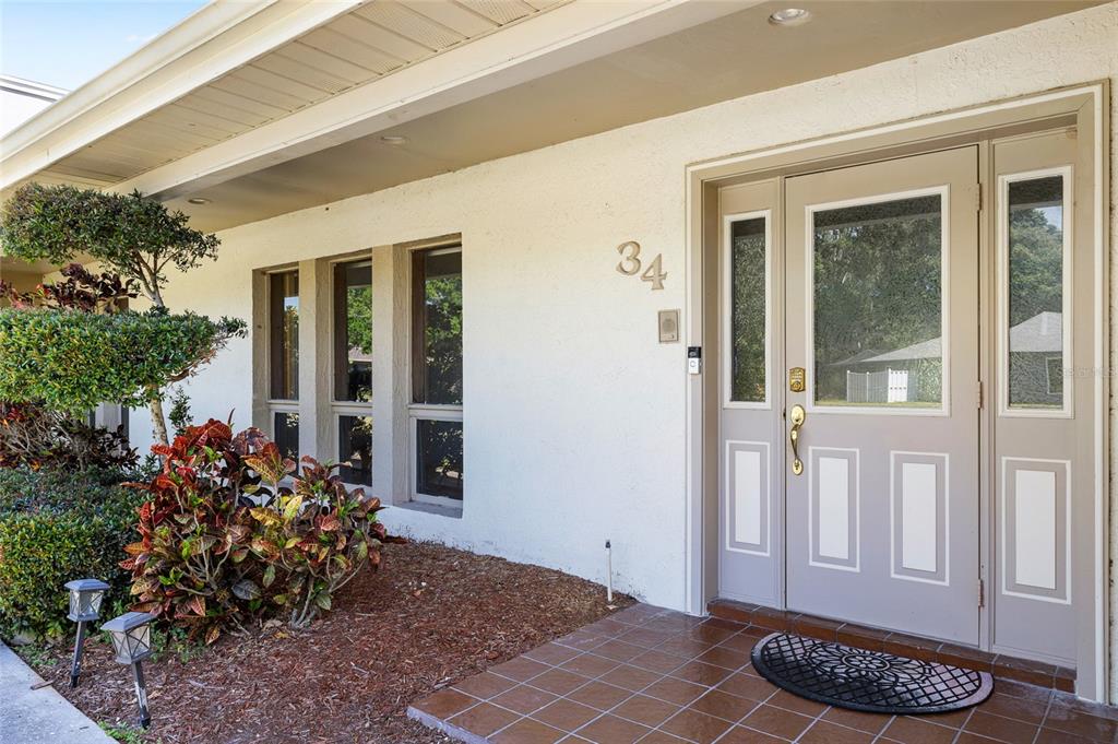 The exterior of a home features a white stucco wall, a front door, and landscaping — 34 MISTY MEADOW LANE, MULBERRY, FL