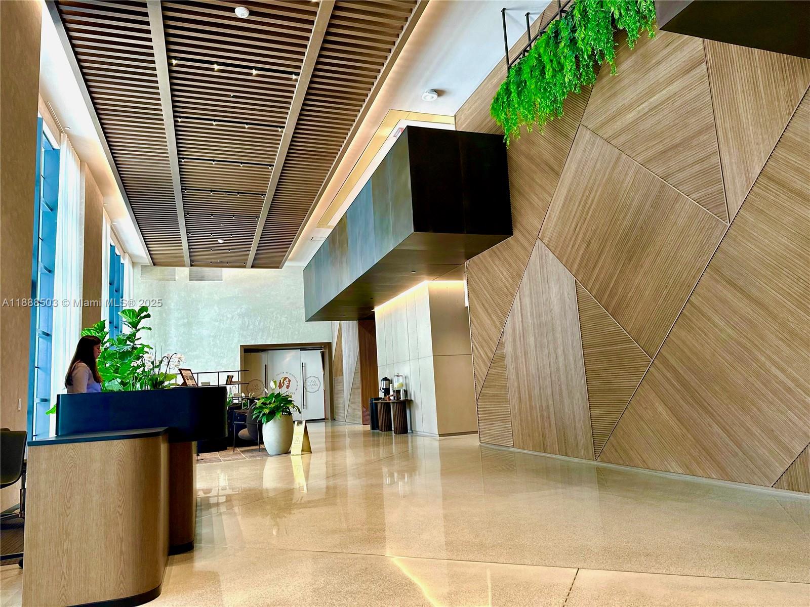 A modern lobby features a slatted wood ceiling, geometric wood wall paneling, and a reception desk — 159 NE 6th St # 3306, Miami FL 33132, MIAMI, FL
