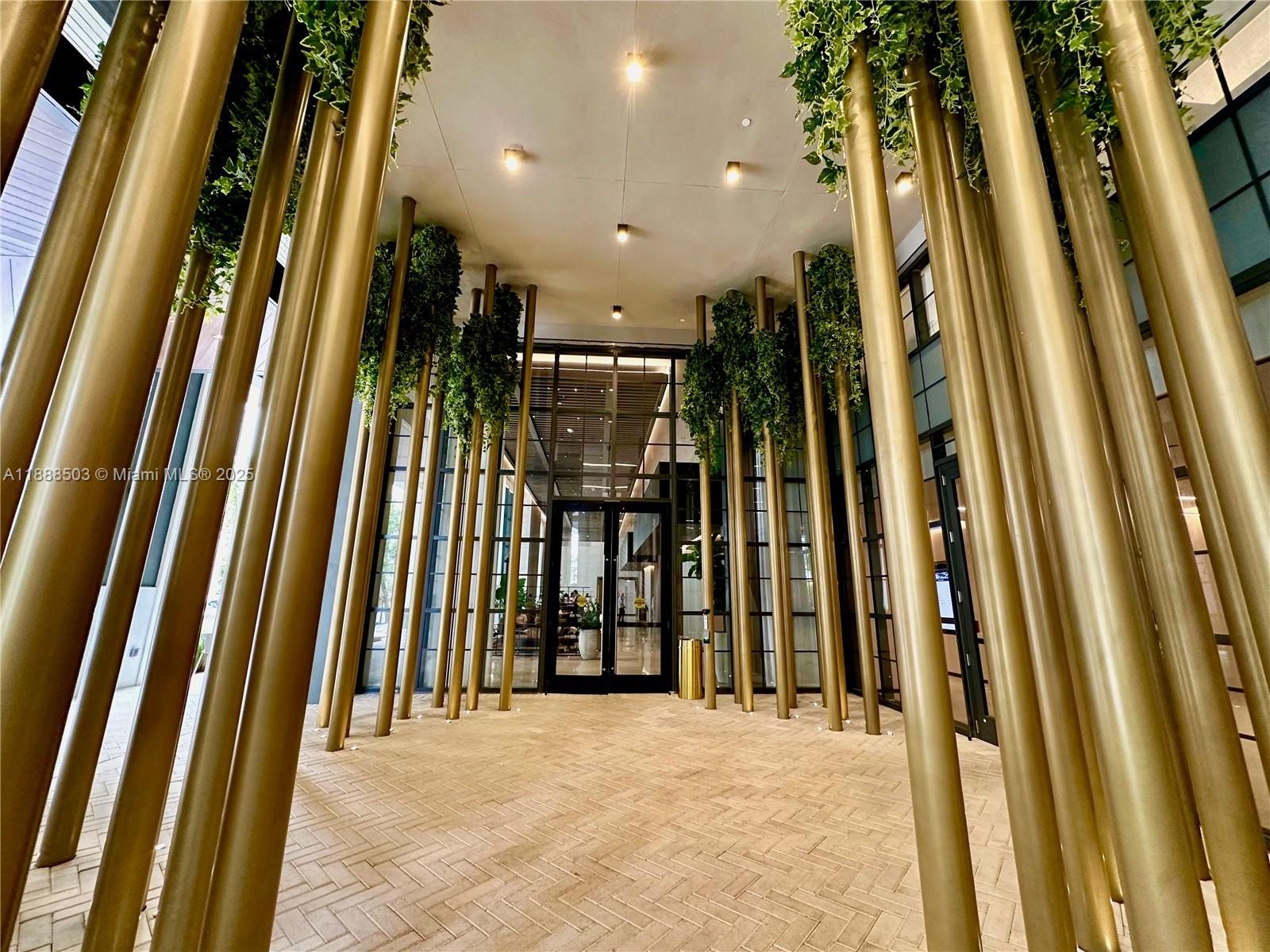 A covered entrance features gold cylindrical columns and hanging greenery over a brick walkway — 159 NE 6th St # 3306, Miami FL 33132, MIAMI, FL