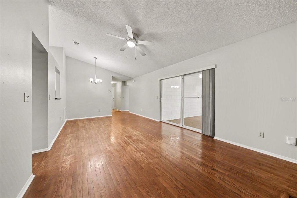 An empty living room features hardwood floors, a vaulted ceiling with a fan, and sliding doors — 7734 LAKESIDE WOODS DRIVE, ORLANDO, FL