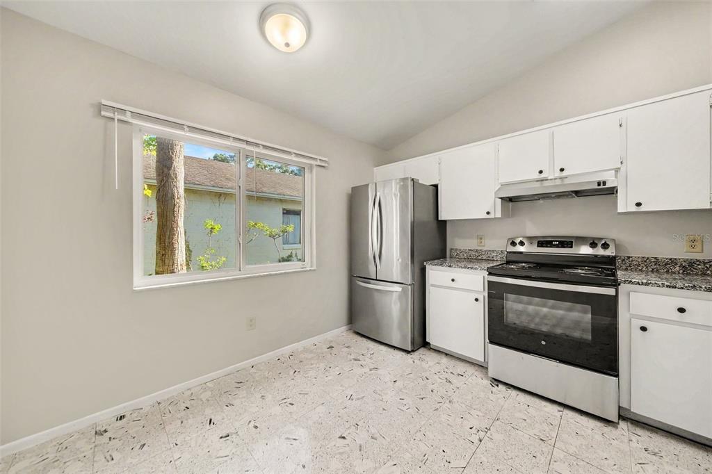 A kitchen with white cabinets, stainless steel appliances, granite countertops, and light-colored tile flooring — 7734 LAKESIDE WOODS DRIVE, ORLANDO, FL