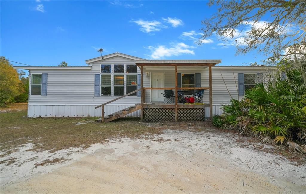 A single-story manufactured home with light gray siding, blue shutters, and a wooden front porch — 137 FRANKLIN AVENUE, POMONA PARK, FL