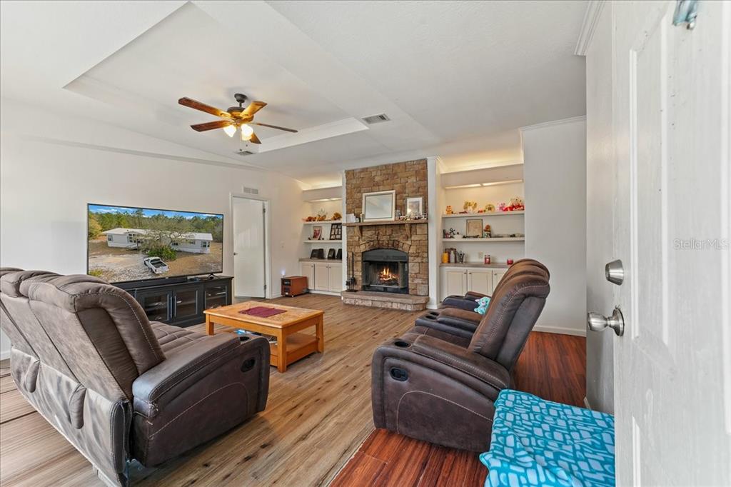 A living room features a stone fireplace, built-in shelving, wood-look flooring, and a ceiling fan — 137 FRANKLIN AVENUE, POMONA PARK, FL