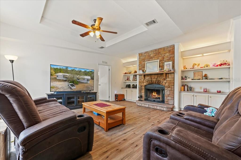 A living room features a stone fireplace, wood-look flooring, and two brown leather reclining sofas — 137 FRANKLIN AVENUE, POMONA PARK, FL