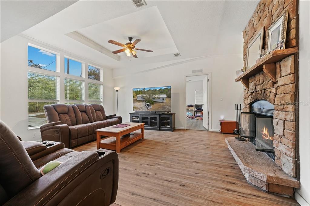 A living room features a stone fireplace, wood-look flooring, a ceiling fan, and large windows — 137 FRANKLIN AVENUE, POMONA PARK, FL