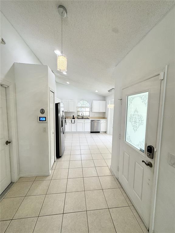 A white-tiled entryway leads into a kitchen with white cabinetry and stainless steel appliances — 2627 ONEIDA LOOP, KISSIMMEE, FL