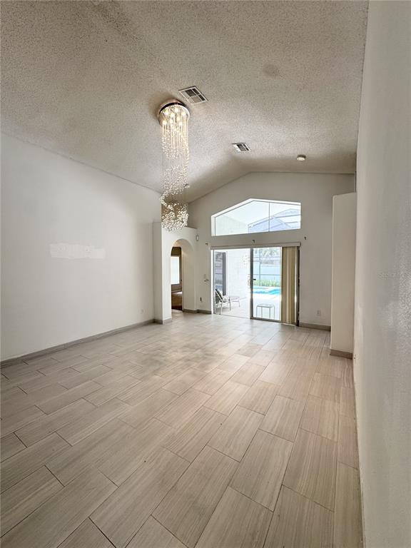A living room features vaulted ceilings, a crystal chandelier, and light-colored tile flooring — 2627 ONEIDA LOOP, KISSIMMEE, FL