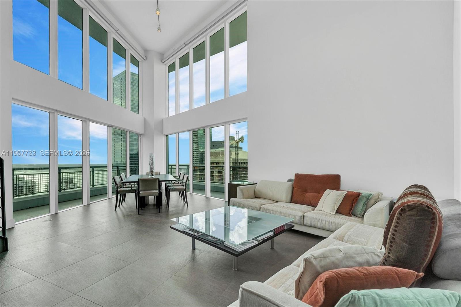 A spacious living and dining area features double-height windows, tile flooring, and modern furniture — 60 SW 13th St # 3400, Miami FL 33130, MIAMI, FL