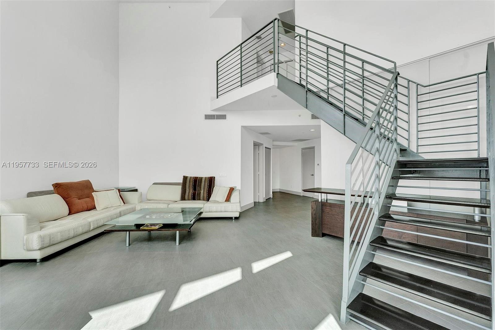 A modern living room features a high ceiling, white walls, gray tile floors, and stairs — 60 SW 13th St # 3400, Miami FL 33130, MIAMI, FL