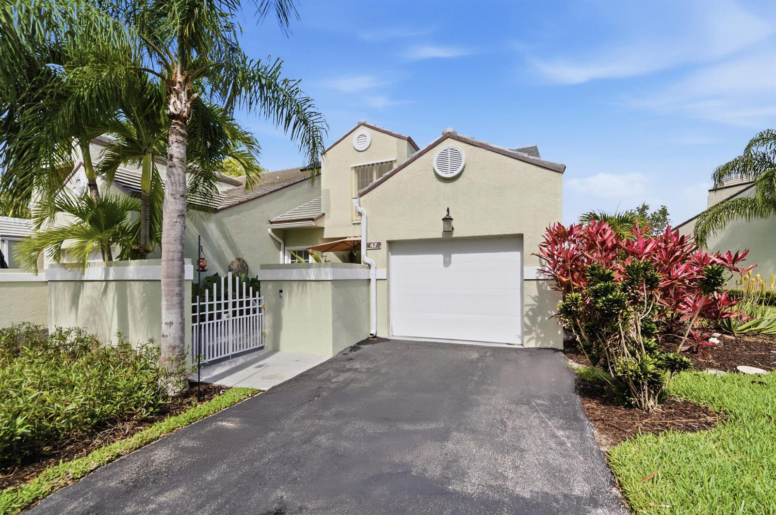 A light-colored house with a single-car garage, a gated courtyard, and a palm tree — 47 N Lakeshore Drive, Hypoluxo FL 33462, HYPOLUXO, FL