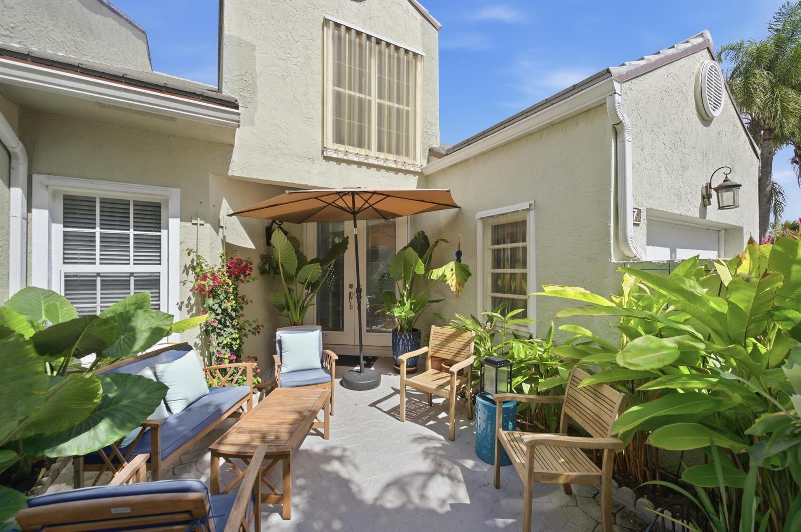 A patio with outdoor furniture, a tan umbrella, and potted plants against a stucco house — 47 N Lakeshore Drive, Hypoluxo FL 33462, HYPOLUXO, FL